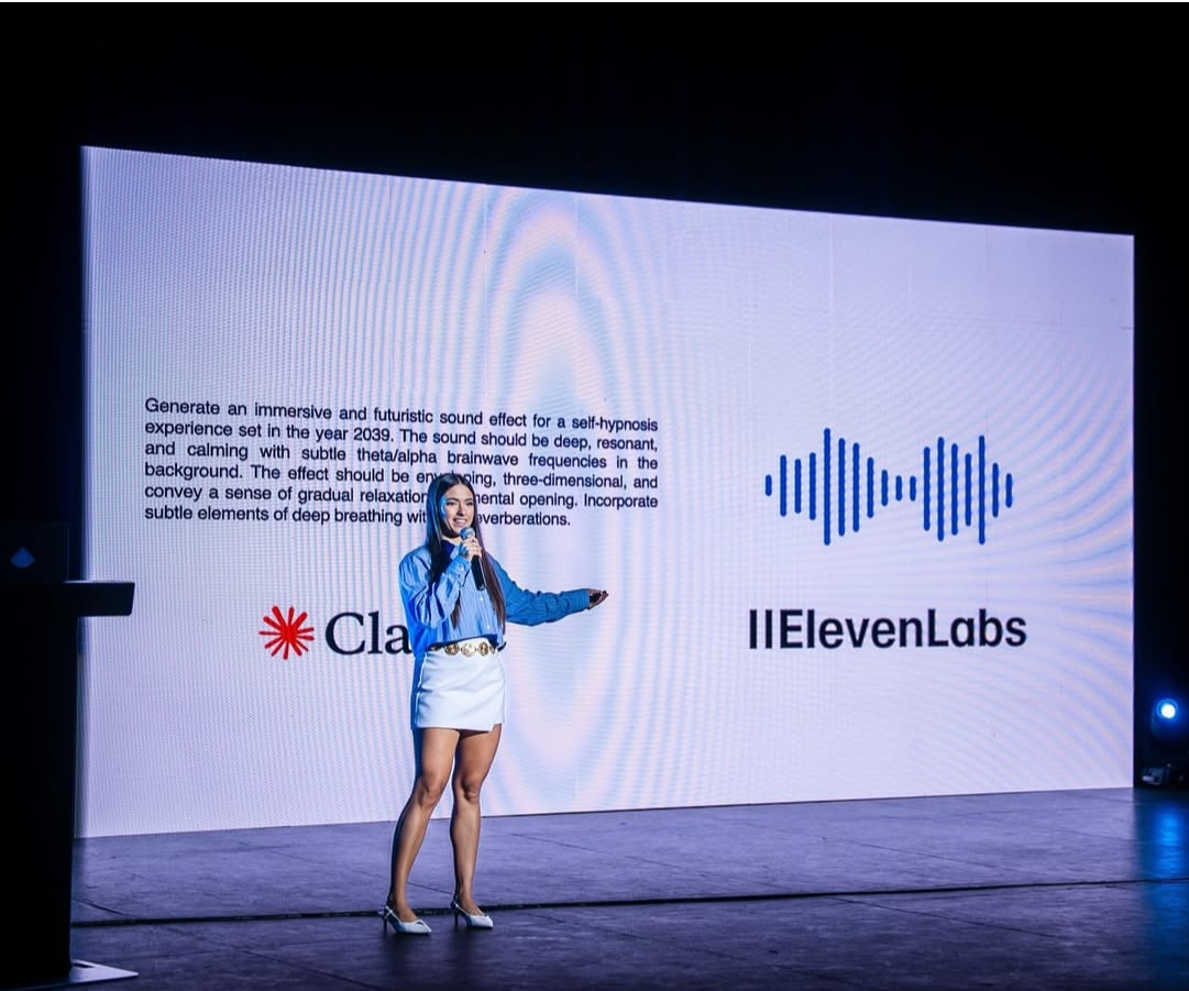 Elsa presentando sobre Claude y ElevenLabs en tarima con pantalla LED